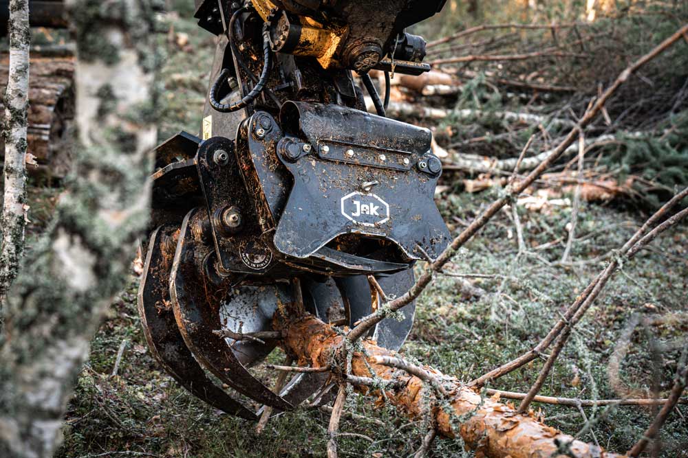 Grappin coupeur d'énergie JAK-300B coupant à travers des pins sur un site d'exploitation forestière.